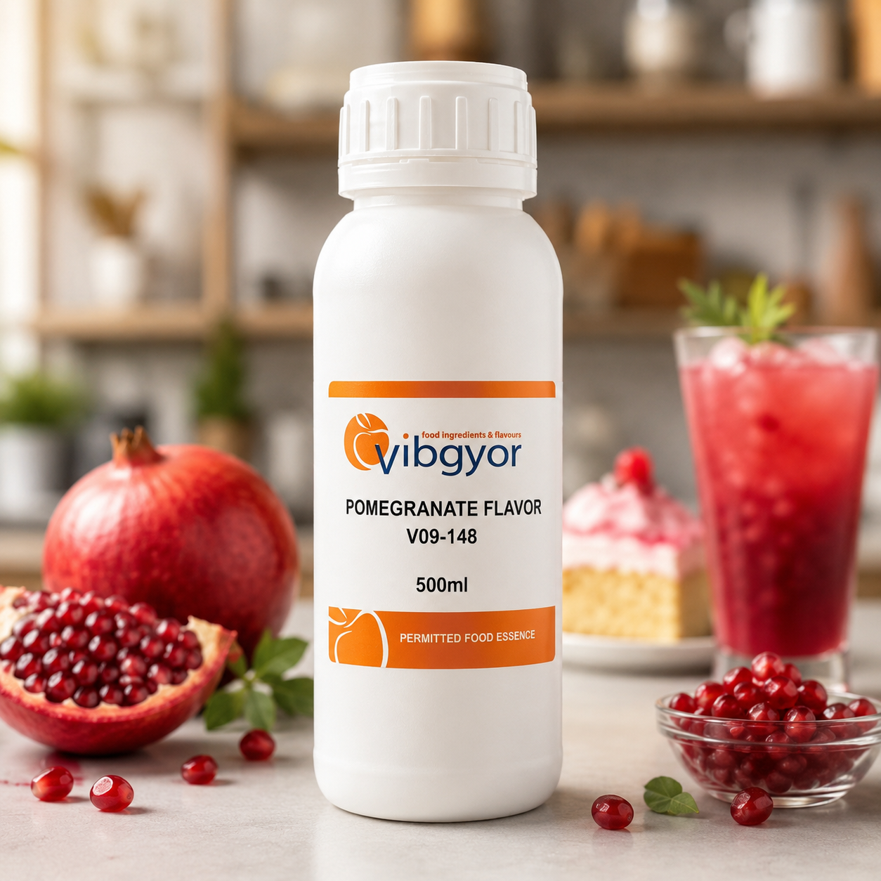 A white plastic bottle of Vibgyor Pomegranate Flavor food essence, 500ml, displayed on a kitchen counter with fresh pomegranates, a glass of red drink, and a slice of cake in the background.