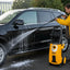 Person using a pressure washer to clean a yellow car outdoors.