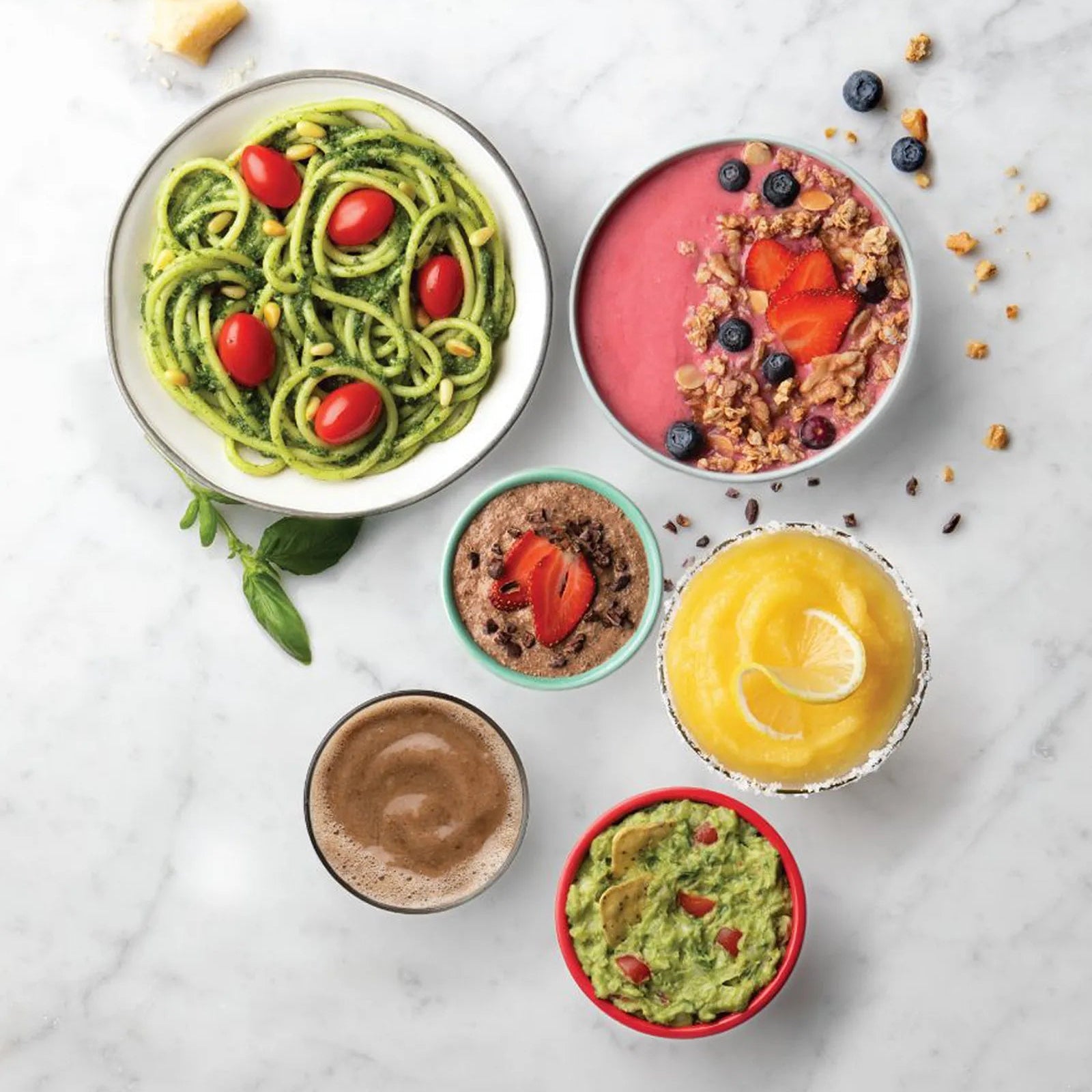 Assorted healthy dishes including pasta, smoothie bowl, and dips on a marble surface