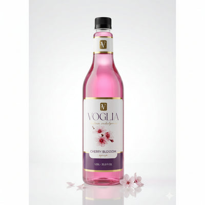 A bottle of Voglia Cherry Blossom syrup with pink liquid, a white and purple label with cherry blossom illustrations, and a black cap, set against a clean white background with decorative cherry blossom petals at the base.
