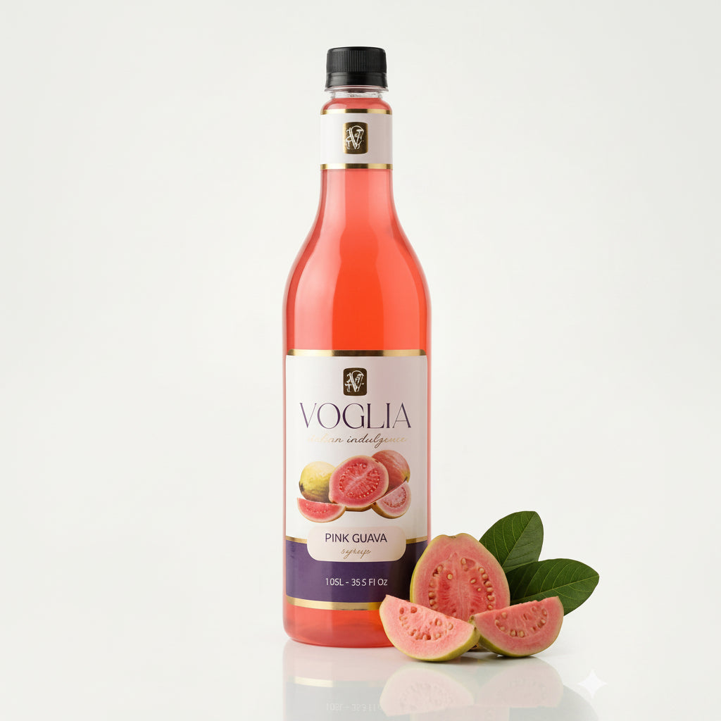 A bottle of Voglia Pink Guava syrup with a black cap, shown next to fresh pink guava slices and green leaves on a clean white background.