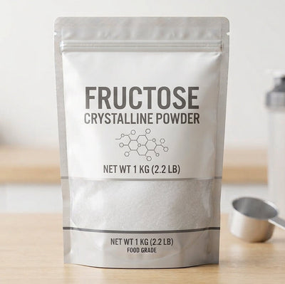 A stand-up pouch of Fructose Crystalline Powder on a wooden surface, with a shaker bottle and scoop blurred in the background.