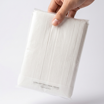 A hand holding a packaged stack of white ultra-soft daily facial tissues against a clean white background. The packaging is clear plastic with printed text reading 'ULTRA-SOFT DAILY FACIAL TISSUES' and 'PREMIUM PLY'.