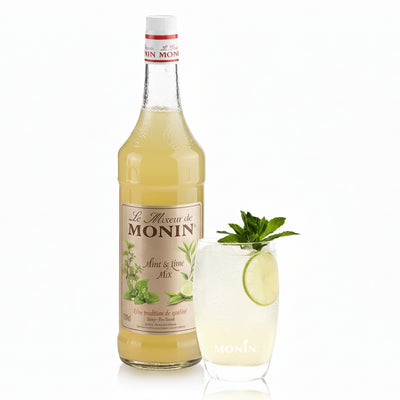 Monin syrup bottle with a glass of lime and mint cocktail on a white background