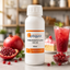 A white plastic bottle of Vibgyor Pomegranate Flavor food essence, 500ml, displayed on a kitchen counter with fresh pomegranates, a glass of red drink, and a slice of cake in the background.
